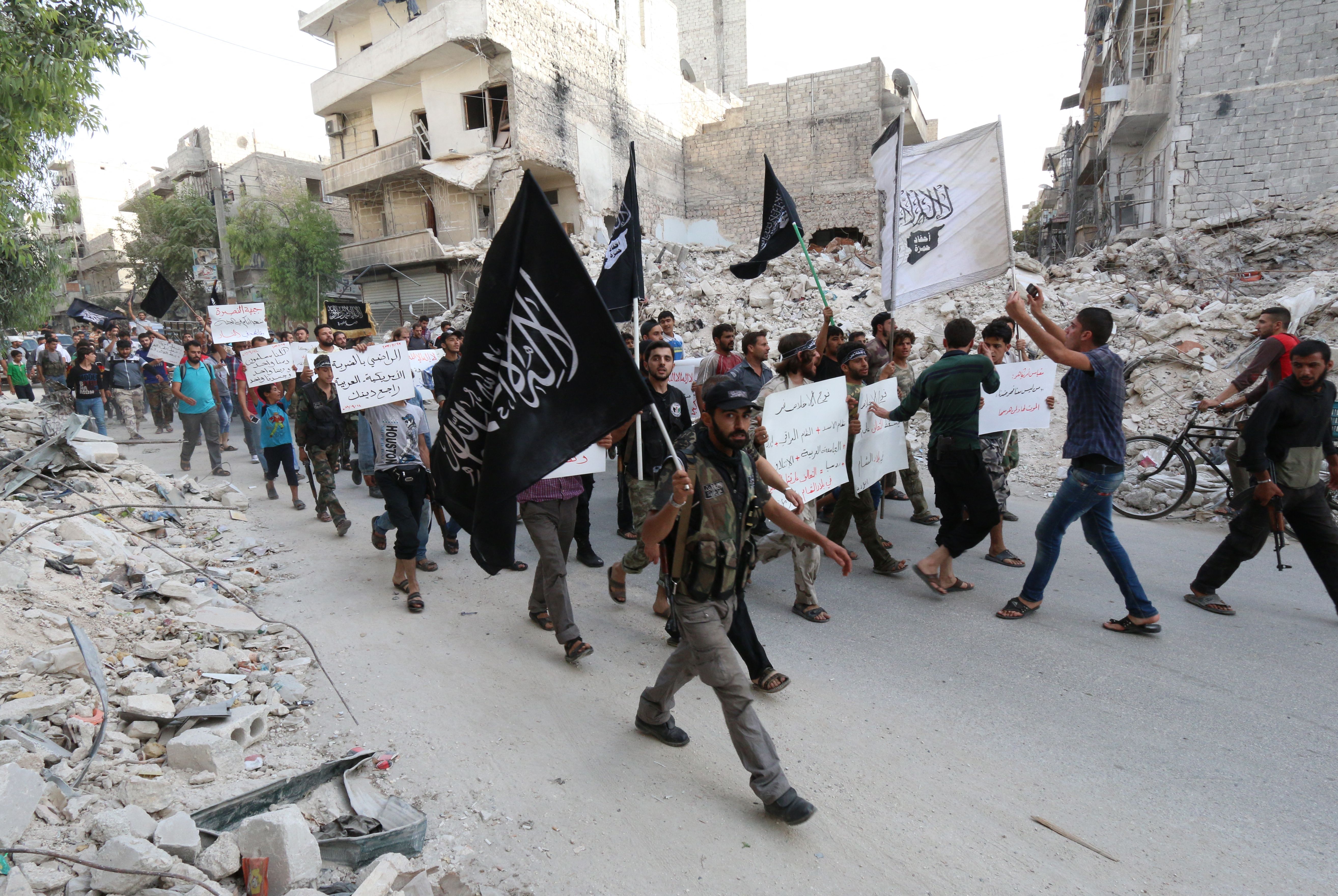 Des partisans du Front Al-Nosra, affilié syrien d'Al-Qaïda, brandissent des drapeaux et pancartes hostiles à Bachar al-Assad et dénonçant les États arabes qui luttent contre Daech lors d'une manifestation à Alep, en septembre 2014.